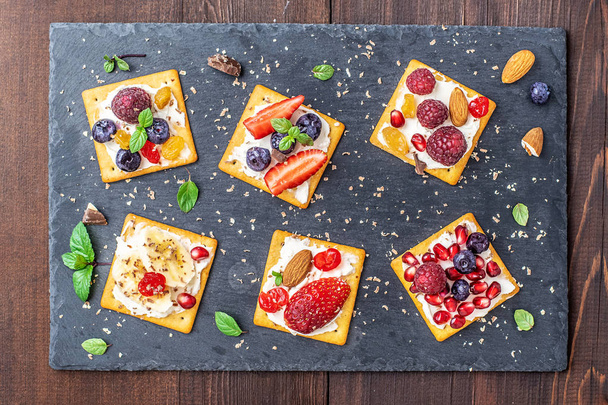 Set of crackers with various fruit close-up on black stone plate. - 写真・画像
