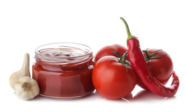 Salsa roja en un frasco e ingredientes frescos, tomates, pimientos y ajo sobre un fondo blanco aislado. Salsa de tomate. Ketchup.
 - Foto, imagen