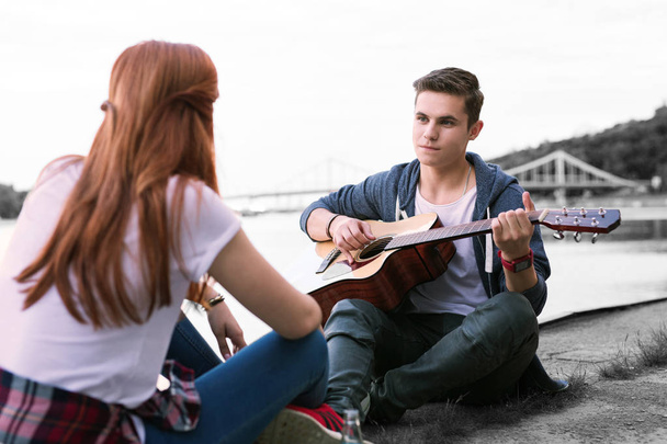 Handsome boy singing the song for his girlfriend sitting near the bridge - 写真・画像