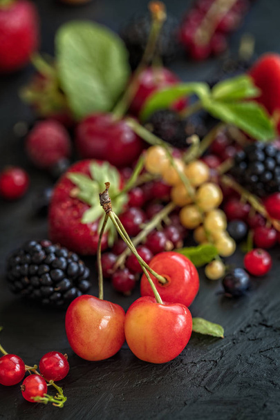 Vegyes bogyók a sötét háttéren kijelölt hangsúlyt. Eper, málna, szeder, cseresznye, piros és sárga áramlatok. Egészséges élet- és tápláló étel fogalmát. Függőleges összetétele  - Fotó, kép