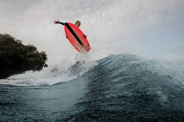 Menino adolescente pulando no wakeboard laranja tendo verão saudável no rio no fundo do céu e árvores
 - Foto, Imagem