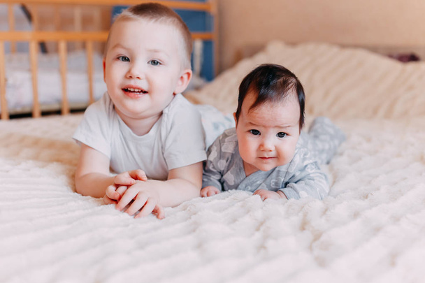 niedliche kleine vier Monate alte Mädchen und ihr älterer Bruder, spielen unter Bettdecke zu Hause im Bett im Schlafzimmer und lächeln glücklich - Foto, Bild