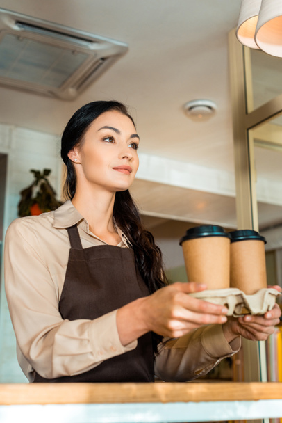 low angle view of brunette waitress holding coffee in paper cups in cafe - Fotoğraf, Görsel