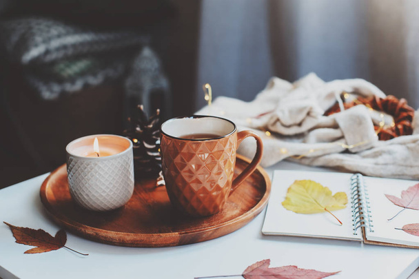 cozy autumn or winter morning at home. Still life details with cup of tea, candle, sketch book with herbarium and warm sweater. Scandinavian hygge concept - Фото, зображення