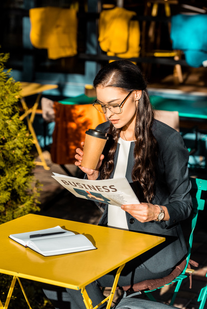 donna attraente che tiene il caffè per andare e leggere il giornale d'affari mentre seduto sulla terrazza del caffè
 - Foto, immagini