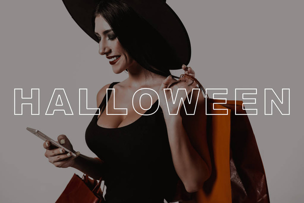 Halloween. Sexy. Half-Turn. Smartphone. Young Woman. Sale. Black Dress. Witch Hat. Packages. Studio. Magic. Fun. Fashion. Pretty. Lady. Glamour. Makeup. Wizard. Stylish. Shop Space. Gothic. Cosmetic. - Photo, image