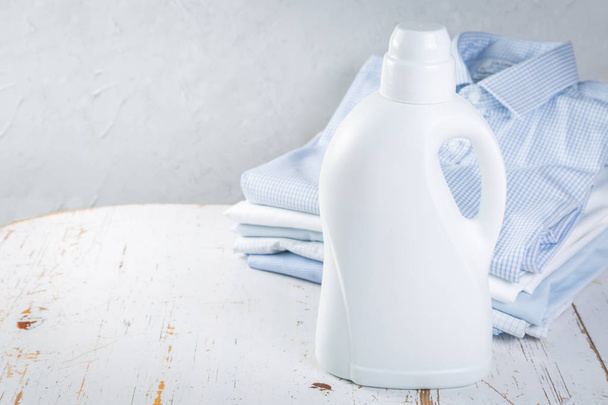 Washing concept - pile of folded shirts with bottle of washing detergent - Fotografie, Obrázek