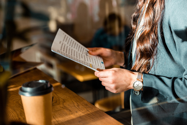 cropped view of businesswoman reading document at cafe with coffee to go - Zdjęcie, obraz