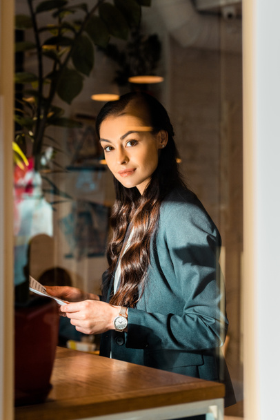 attraktive brünette Geschäftsfrau in schwarzer Jacke hält Zeitung im Café  - Foto, Bild