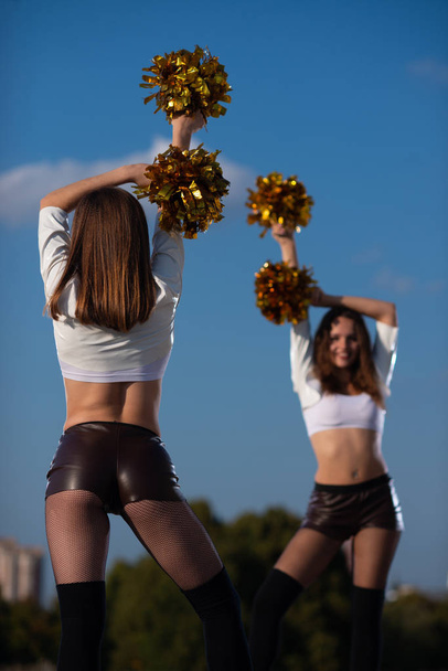 Two girls cheerleaders with pompons dancing outdoors on sky background - Foto, Imagen