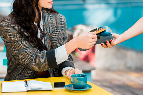 Ausgeschnittene Ansicht einer Frau, die mit Kreditkarte am Zahlungsterminal im Café bezahlt - Foto, Bild