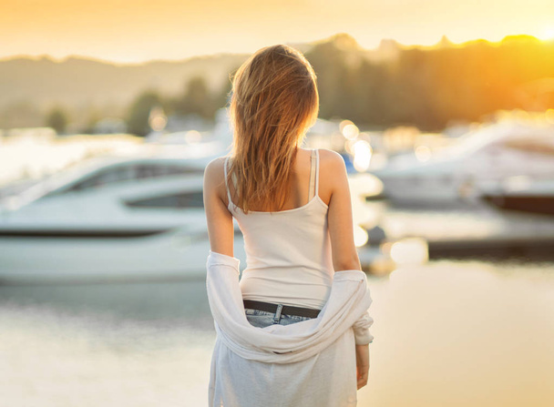 Young girl on the background of boats. Sunset in the Yacht Club. Gorgeous warm bokeh. - Foto, imagen
