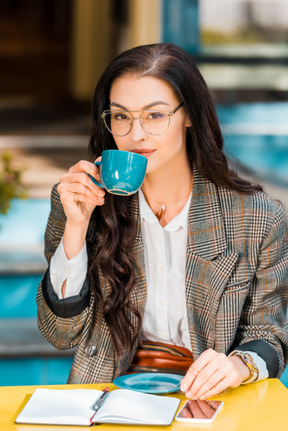 приваблива жінка п'є каву на терасі ресторану з планувальником та смартфоном
 - Фото, зображення