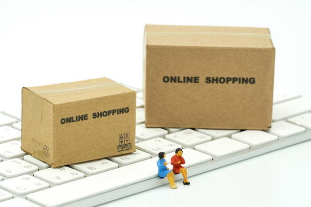 Miniatur zwei Personen sitzen auf weißer Tastatur Online-Shopping mit einem Warenkorb und Einkaufstaschen Lieferservice mit als Hintergrund Einkaufskonzept und Lieferservice-Konzept mit Kopierraum - Foto, Bild