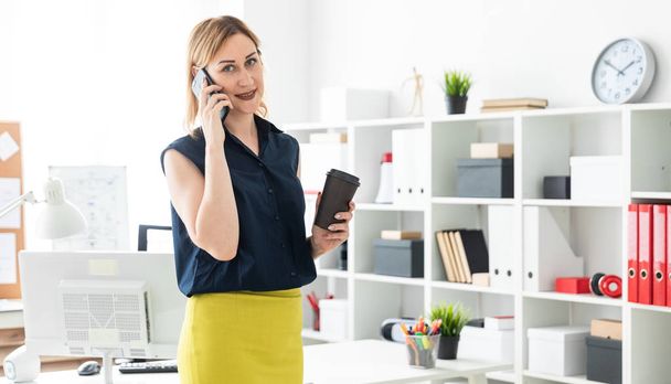 молодая деловая женщина разговаривает по телефону в офисе и держит чашку кофе
 - Фото, изображение
