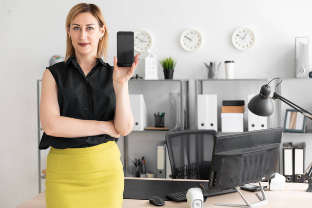 mladá podnikatelka stojící v kanceláři a ukazuje displej telefonu - Fotografie, Obrázek