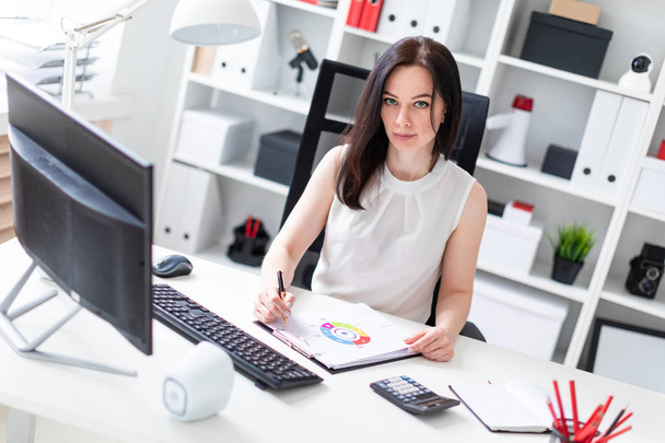 Een jong meisje zittend op kantoor op een computer Desk en werken met documenten en een rekenmachine. - Foto, afbeelding