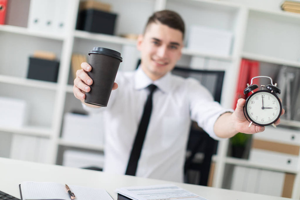 young man sitting at a table in the office and holding a cup  of coffee  - Foto, Bild