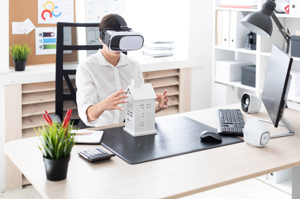 jonge zakenvrouw zittend in virtual reality bril. Voor haar op tafel ligt de indeling van het huis. - Foto, afbeelding