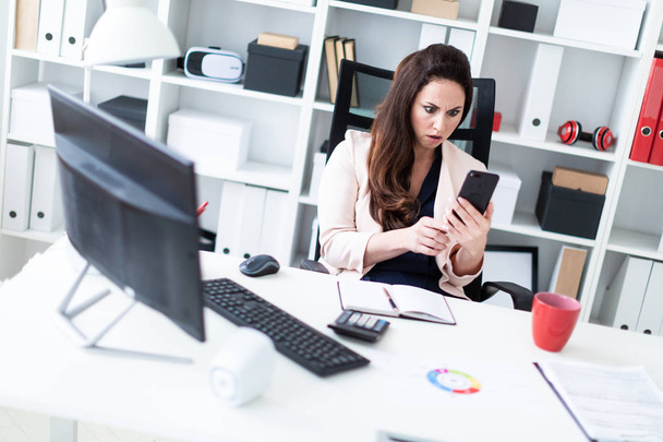 young businesswoman sitting at a computer and holding a phone  - Foto, imagen