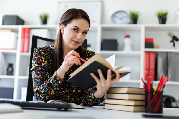 экономист с ручкой в руке внимательно читает бизнес-книгу и сидит за столом в светлом офисе
  - Фото, изображение