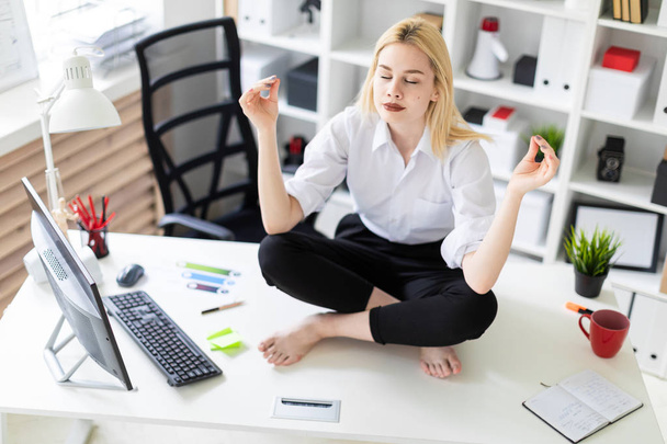 молодая деловая женщина сидит и медитирует на столе в офисе
. - Фото, изображение