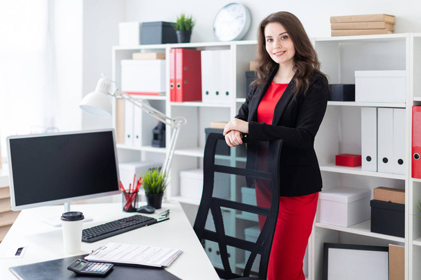 Beautiful young girl working in a bright office. A young girl in a red dress and a black jacket.  - 写真・画像
