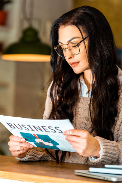 attractive brunette woman reading business newspaper at restaurant  - Foto, imagen