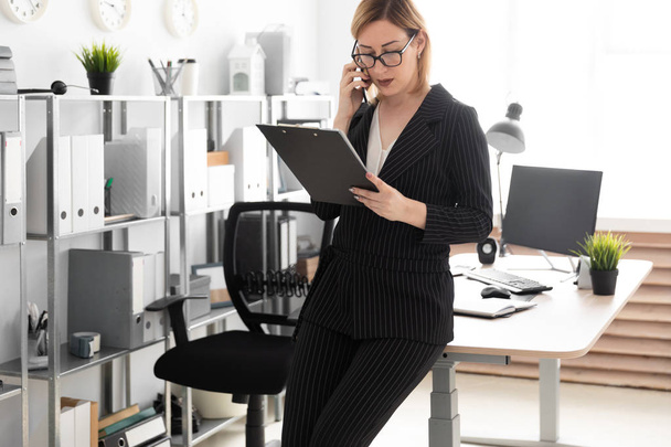 молодая деловая женщина, стоящая в офисе и разговаривающая по телефону
 - Фото, изображение