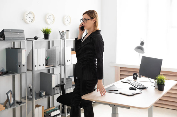 молодая деловая женщина, стоящая в офисе и разговаривающая по телефону
 - Фото, изображение