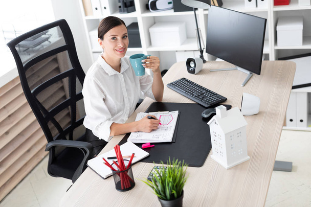  schöne junge Geschäftsfrau mit Kaffee, die in einem hellen Büro arbeitet. Sie hat dunkle Haare. Er trägt ein weißes Hemd.  - Foto, Bild