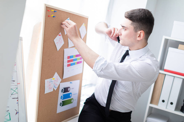 Een jonge man in het kantoor permanent in de buurt van het bord met stickers en praten over de telefoon - Foto, afbeelding