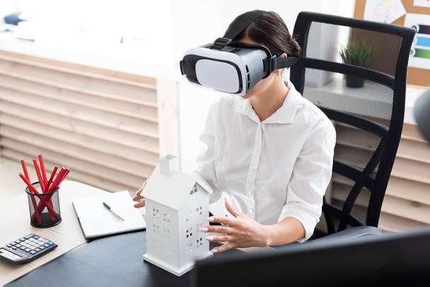 jonge zakenvrouw zittend in virtual reality bril. Voor haar op tafel ligt de indeling van het huis. - Foto, afbeelding