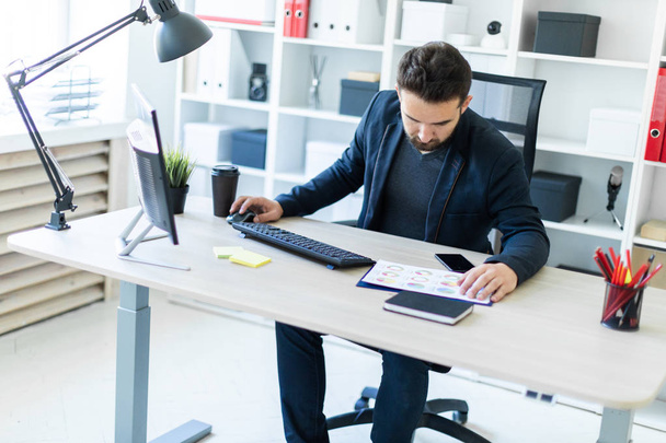 Młody człowiek pracuje w biurze przy komputerze biurko z dokumentów, diagramy i telefon. - Zdjęcie, obraz