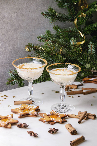 Eggnog Christmas milk cocktail, served in two vintage crystal glasses with shortbread star shape sugar cookies, cinnamon sticks, fir branch over white marble table. - Foto, afbeelding