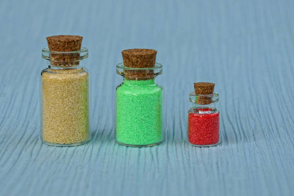 Tři skleněné uzavřené lahve s barevným pískem na stůl - Fotografie, Obrázek