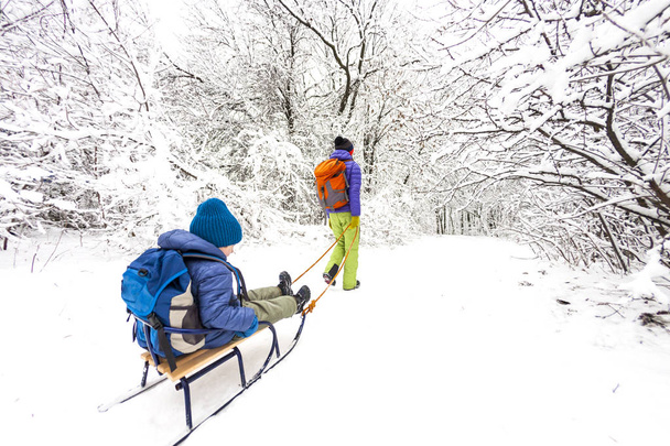 Una mujer lleva a un niño en un trineo. Mamá camina con su hijo en el camino de la nieve. Felices vacaciones de invierno. Diversión invernal. Bebé en el trineo
. - Foto, imagen