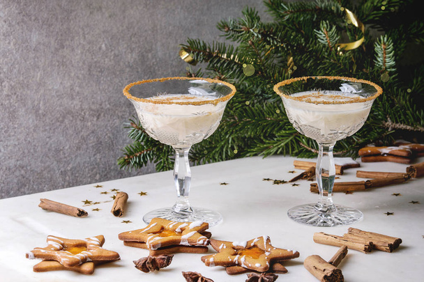 Eggnog Christmas milk cocktail, served in two vintage crystal glasses with shortbread star shape sugar cookies, cinnamon sticks, fir branch over white marble table. - Фото, зображення