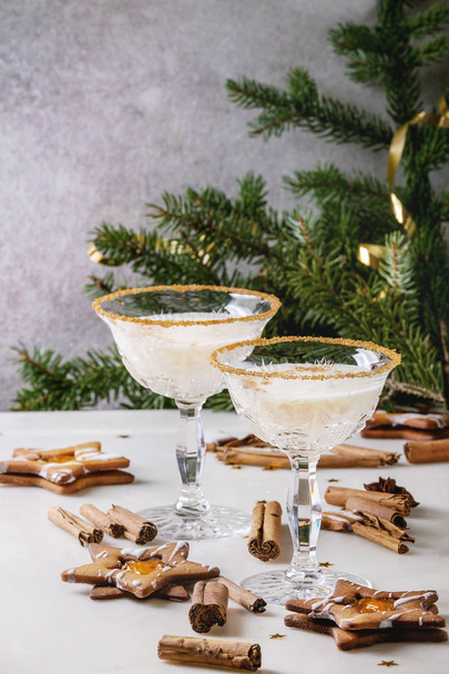 Eggnog Christmas milk cocktail, served in two vintage crystal glasses with shortbread star shape sugar cookies, cinnamon sticks, fir branch over white marble table. - Foto, Bild