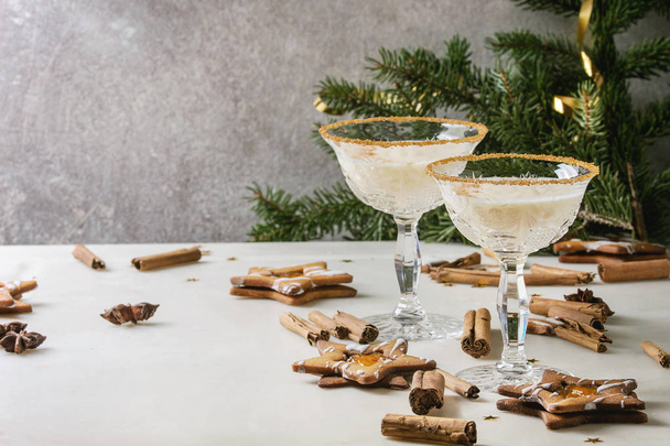 Eggnog Christmas milk cocktail, served in two vintage crystal glasses with shortbread star shape sugar cookies, cinnamon sticks, fir branch over white marble table. - Foto, Imagen