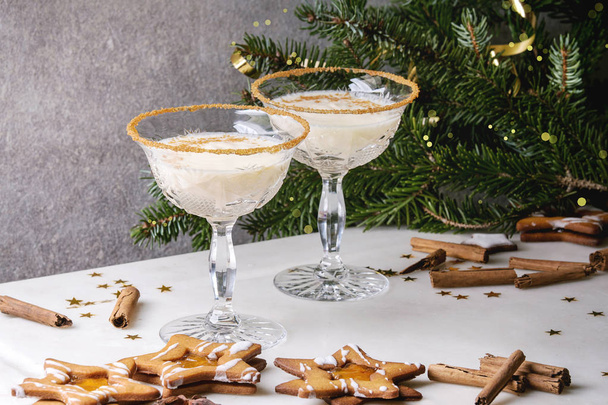 Eggnog Christmas milk cocktail, served in two vintage crystal glasses with shortbread star shape sugar cookies, cinnamon sticks, fir branch over white marble table. - Foto, Imagen