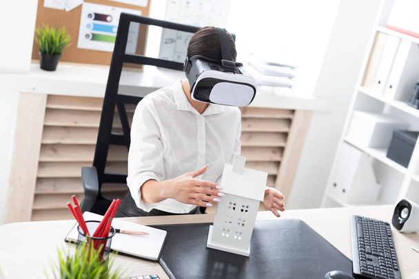 young businesswoman sitting in virtual reality glasses. Before her on the table is the layout of the house - Photo, image