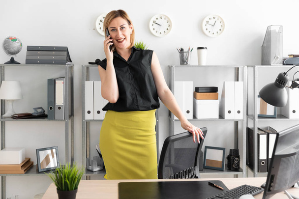 joven mujer de negocios de pie en la oficina y hablando por teléfono
 - Foto, Imagen