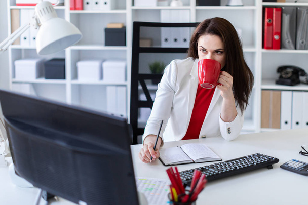 jovem empresária no escritório perto da mesa, segurando uma caneca vermelha
 - Foto, Imagem