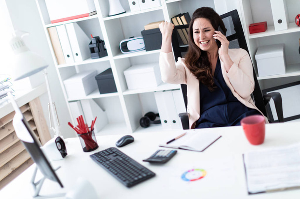 young businesswoman sitting at a computer and holding a phone  - Foto, Bild