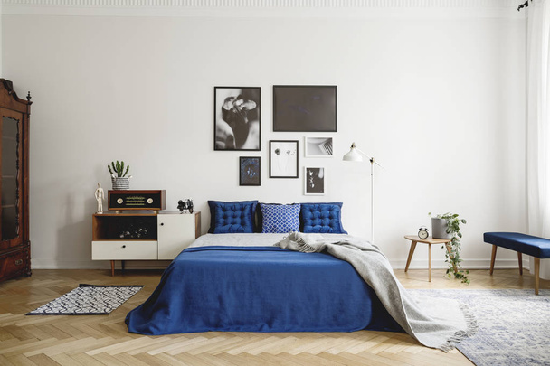 Vintage bedroom interior with bedside table, king size bed with blue bedding and pillows. Mockup gallery on the white wall. Real photo concept - Foto, Imagen