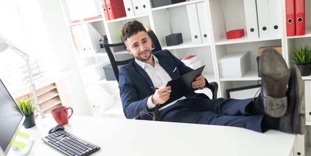 Mladý muž stojící u stolu v kanceláři, telefonování a psaní textu na klávesnici. - Fotografie, Obrázek
