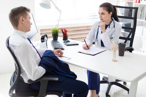 врач опрашивает молодого пациента, сидя за столом в офисе
  - Фото, изображение