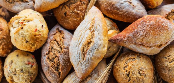 Различные виды свежего хлеба на деревянном столе. Изолированный ассортимент хлеба на коричневом фоне
. - Фото, изображение