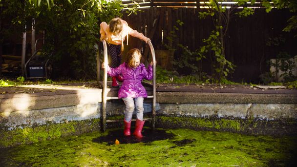 Kislány ül egy fém létra és a lógó lábát a régi medence - Fotó, kép